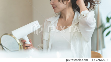 A woman blow-drying her hair with a hair dryer (hair care) 135266805