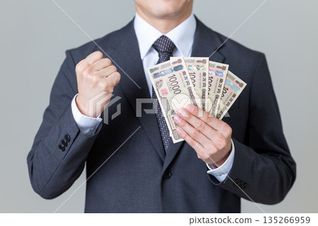 一位身穿西裝的中年男商人,手持鈔票,揮舞著拳頭 一位身穿西裝的中年男商人,手持鈔票,揮舞著拳頭 135266959