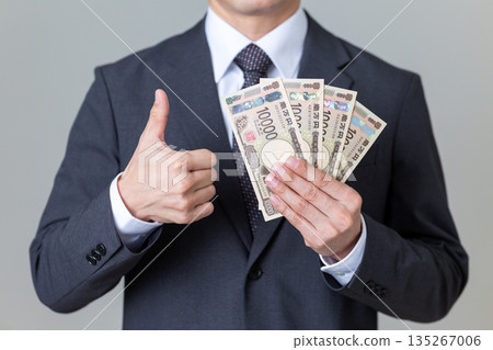 A middle-aged male businessman in a suit holding money and giving a thumbs up 135267006