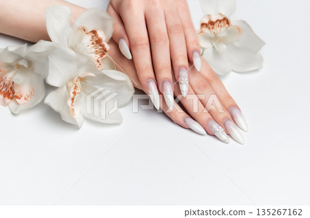 Elegant hands displaying long white almond nails with orchid flowers 135267162