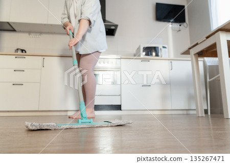 Woman performing housework, mopping kitchen floor for hygiene and cleanliness in a modern domestic setting Woman performing housework, mopping kitchen floor for hygiene and cleanliness in a modern domestic setting 135267471