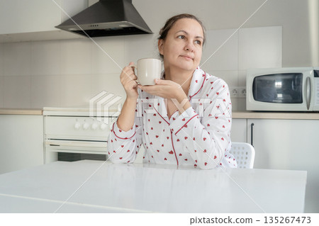 Woman in heart-patterned pajamas drinking coffee in her kitchen, enjoying a moment of solitude and reflection Woman in heart-patterned pajamas drinking coffee in her kitchen, enjoying a moment of solitude and reflection 135267473