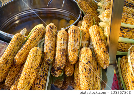 Close-up of grilled corn on the cob, a popular street food snack, ready to eat. The golden-brown kernels are delicious. Close-up of grilled corn on the cob, a popular street food snack, ready to eat. The golden-brown kernels are delicious. 135267868