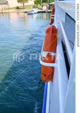 View from a boat with an orange life preserver, the water, and a shoreline in the background. View from a boat with an orange life preserver, the water, and a shoreline in the background. 135267869