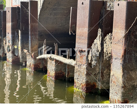 Rusty metal pillars in water showing decay and erosion effects. Rusty metal pillars in water showing decay and erosion effects. 135267894