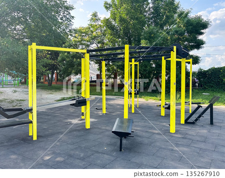Outdoor gym equipment in a park with trees and clear sky. Outdoor gym equipment in a park with trees and clear sky. 135267910