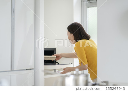 A woman in her 50s warming up her lunch in the microwave 135267943