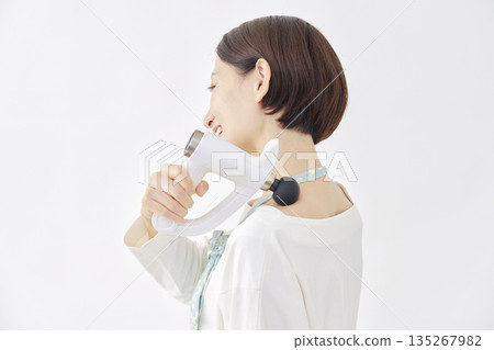Woman wearing an apron using a massage gun, stiff shoulders, white background 135267982