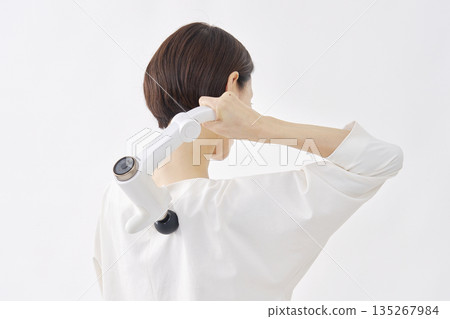 Woman using a massage gun, stiff shoulders, white background 135267984