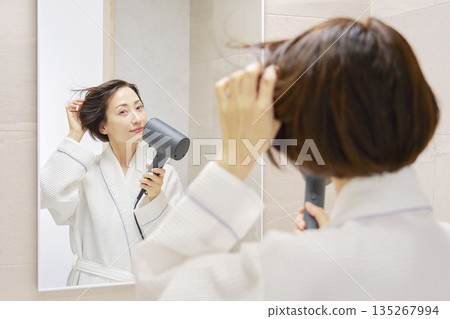 婦女用吹風機烘乾她的頭髮。 135267994
