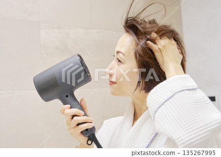婦女用吹風機烘乾她的頭髮。 135267995