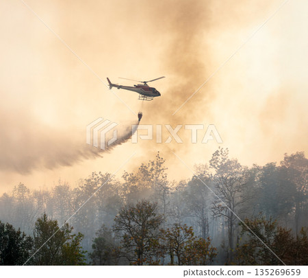Fire fighting helicopter dropping water to put out a forest fire. Fire fighting helicopter dropping water to put out a forest fire. 135269659