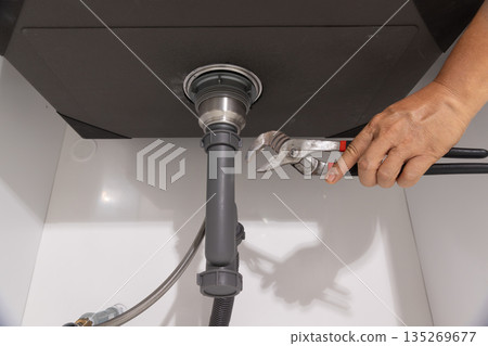 Plumber fixing drain clog under sink. 135269677