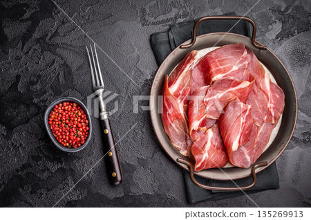 Thin slices of Speck, Jambon Italian cured meat. black background. top view Thin slices of Speck, Jambon Italian cured meat. black background. top view 135269913