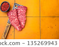 Raw denver steak, displaying its vibrant hue and marbling. Perfectly suited for quick cooking methods that bring out its natural taste. orange background. top view 135269943