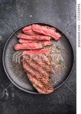 Grilled New York Striploin steak, perfectly seared with beautiful grill marks, showcasing its juicy tenderness and rich flavor. black background. top view Grilled New York Striploin steak, perfectly seared with beautiful grill marks, showcasing its juicy tenderness and rich flavor. black background. top view 135269948