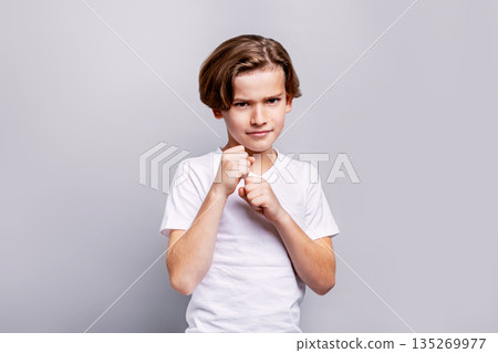 Aggressive Young boy posing in fighting stance with clenched fists, determination and strength in studio against grey isolated background for children character and emotion concepts Aggressive Young boy posing in fighting stance with clenched fists, determination and strength in studio against grey isolated background for children character and emotion concepts 135269977