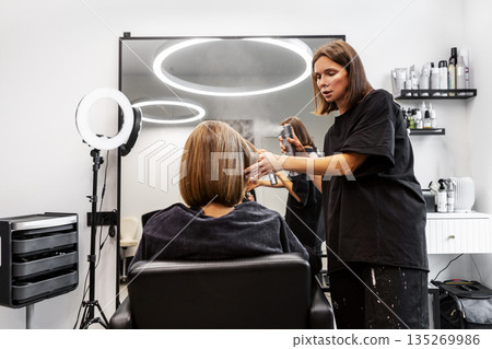 Hairstylist in modern salon styles chic bob haircut, applying hairspray for fixation and perfect hold. Professional beauty service in action 135269986