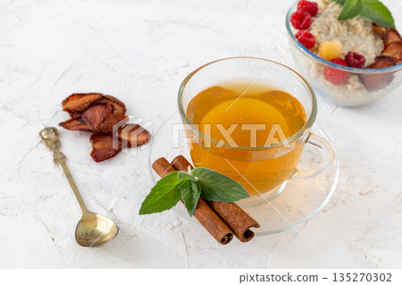 Glass cup of green tea with cinnamon and leaves of mint on a saucer. 135270302