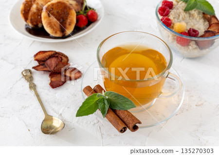 Glass cup of green tea with cinnamon and leaves of mint on a saucer. Glass cup of green tea with cinnamon and leaves of mint on a saucer. 135270303
