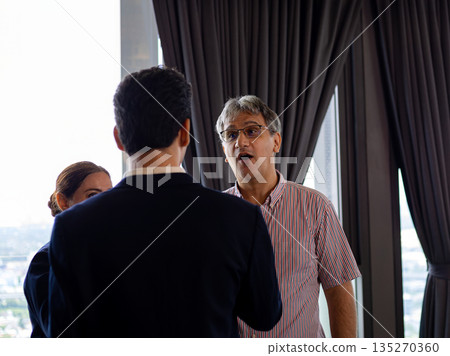 Business professionals engaged in conversation during corporate event, with one man actively speaking, highlighting leadership, communication, and idea sharing in workplace culture 135270360