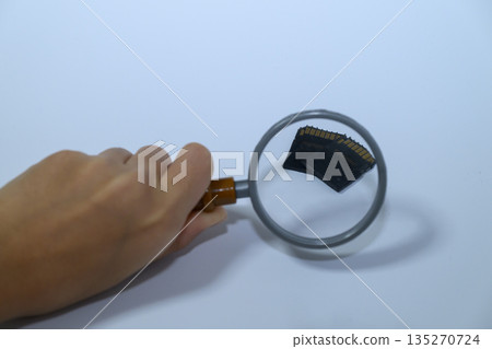 A person inspecting an SD card with a magnifying glass A person inspecting an SD card with a magnifying glass 135270724