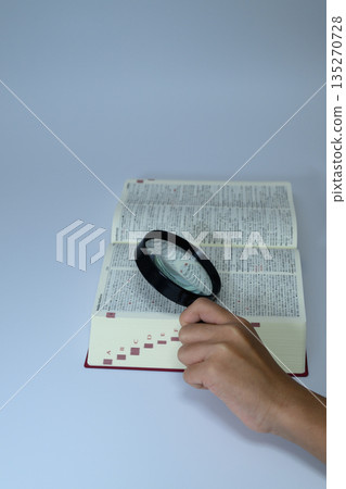 一張豎幅照片，照片中一個人正用放大鏡查閱字典。 135270728