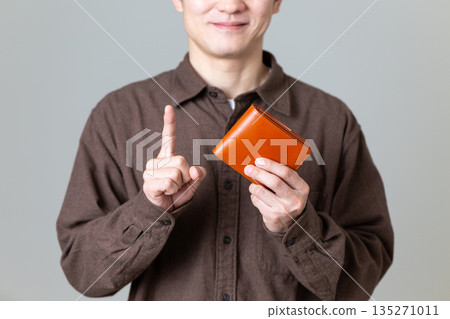 一位身著休閒裝的中年男性商務人士,手裡拿著錢包,食指向上指著。 一位身著休閒裝的中年男性商務人士,手裡拿著錢包,食指向上指著。 135271011
