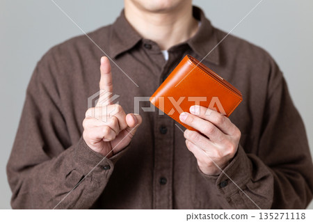 一位身著休閒裝的中年男性商務人士，手裡拿著錢包，食指向上指著。 135271118