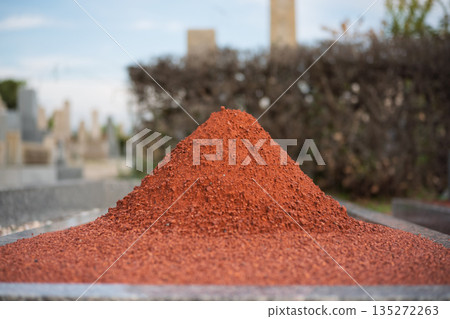 墓園裡，一座墳墓前堆著一堆赤玉土，背景模糊（墓園維護、裝飾用沙、紋理材料） 135272263