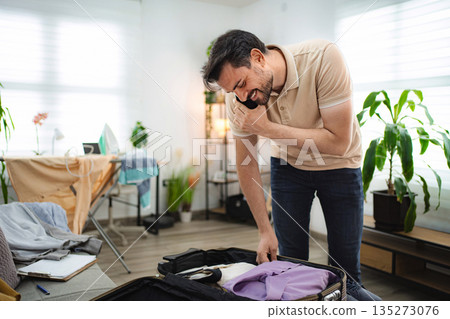 Man talking on the phone while packing his suitcase at home Man talking on the phone while packing his suitcase at home 135273076