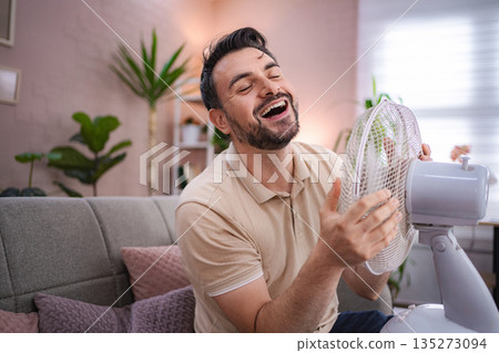 Man refreshing himself with a fan during a heat wave at home Man refreshing himself with a fan during a heat wave at home 135273094