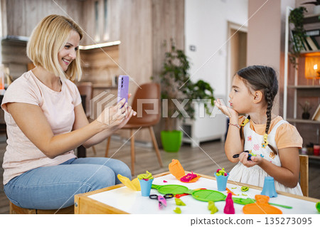 Mother and daughter enjoying creative playtime at home, capturing memories with a smartphone Mother and daughter enjoying creative playtime at home, capturing memories with a smartphone 135273095