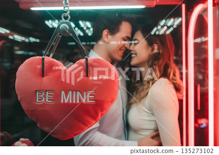 Couple sharing a romantic moment as they win a 'be mine' heart plush from a claw machine, perfect for valentine's day or dating concepts 135273102