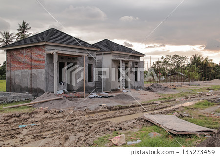 Unfinished houses under construction with overcast sky and muddy ground showing the progress of property development and real estate investment in rural area with natural light Unfinished houses under construction with overcast sky and muddy ground showing the progress of property development and real estate investment in rural area with natural light 135273459