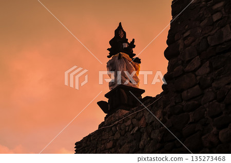 Balinese statue standing atop weathered stone wall at dusk under natural light with copy space offering tranquil cultural backdrop for travel blogs Balinese statue standing atop weathered stone wall at dusk under natural light with copy space offering tranquil cultural backdrop for travel blogs 135273468