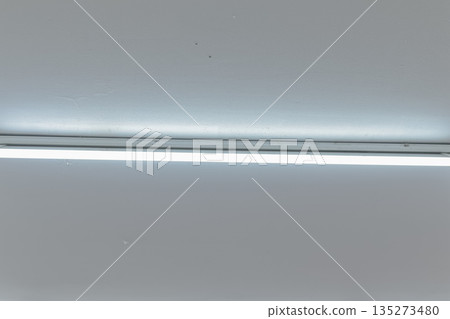 Fluorescent light fixture emitting bright light on a white ceiling with copy space offering minimalist interior design applications Fluorescent light fixture emitting bright light on a white ceiling with copy space offering minimalist interior design applications 135273480