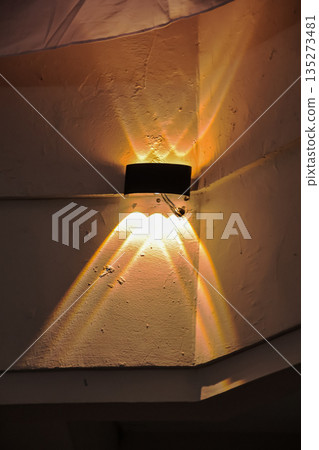 Modern wall lamp emitting rays of warm light on textured wall, creating dramatic shadows for home decor and architectural design with ample copy space 135273481