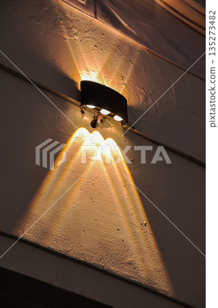 Modern outdoor wall light casting dramatic light patterns on textured surface creating ambient lighting effect in natural light with copy space 135273482
