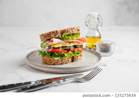 Sandwich with ham, cheese, lettuce, tomatoes, cucumbers and seeded bread on a plate 135273639