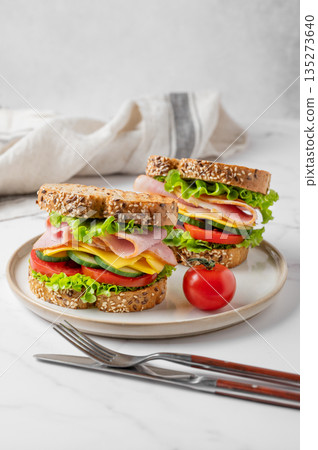 Two sandwiches with ham, cheese, lettuce, vegetables and seeded bread on a plate 135273640