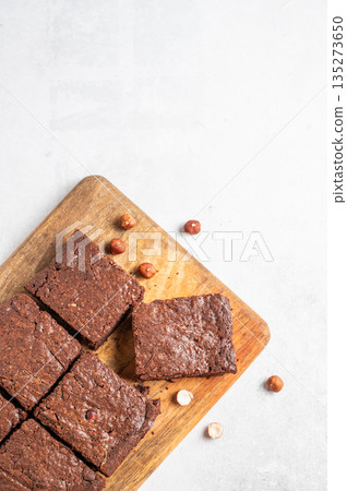Chocolate brownie on a wooden board on a light background with nuts and morning shadow. 135273650