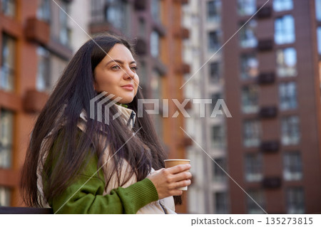 Woman standing on a modern park, drinking coffee and looking thoughtful Woman standing on a modern park, drinking coffee and looking thoughtful 135273815