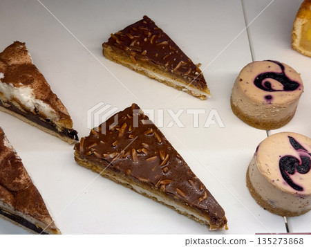 Assorted cake slices and mini cheesecakes in dessert case. Sweet variety, pastry craft, and indulgent choice through gourmet bakery selection Assorted cake slices and mini cheesecakes in dessert case. Sweet variety, pastry craft, and indulgent choice through gourmet bakery selection 135273868