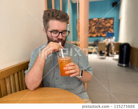 Man drinking iced fruit tea with straw in cafe interior. Urban lifestyle, leisure break, and modern dining experience through casual beverage moment Man drinking iced fruit tea with straw in cafe interior. Urban lifestyle, leisure break, and modern dining experience through casual beverage moment 135273888