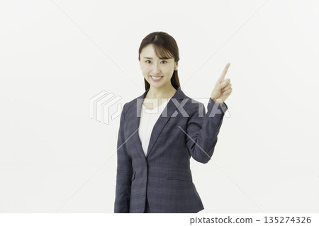 Portrait of a young Japanese woman in a suit looking at the camera and pointing at something on a white background 135274326