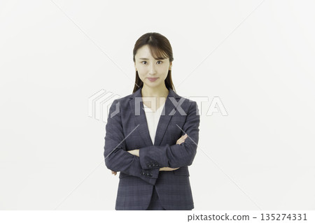Portrait of a young Japanese woman in a suit looking at the camera with her arms crossed on a white background 135274331