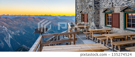 The terrace of Julius Payer House overlooks the stunning Ortler Alps during sunset. Wooden benches line the patio, providing a perfect spot for relaxation and enjoyment of the breathtaking landscape. The terrace of Julius Payer House overlooks the stunning Ortler Alps during sunset. Wooden benches line the patio, providing a perfect spot for relaxation and enjoyment of the breathtaking landscape. 135274524