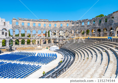 The Roman amphitheatre in Pula showcases ancient architecture, with its stone structure and seats arranged for an event. 135274544