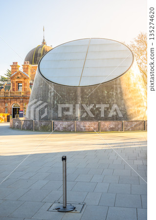 Visitors enjoy the modern design of the Peter Harrison Planetarium in Greenwich, London, as sunlight reflects off the unique dome structure. The planetarium offers educational activities and exhibits. Visitors enjoy the modern design of the Peter Harrison Planetarium in Greenwich, London, as sunlight reflects off the unique dome structure. The planetarium offers educational activities and exhibits. 135274620